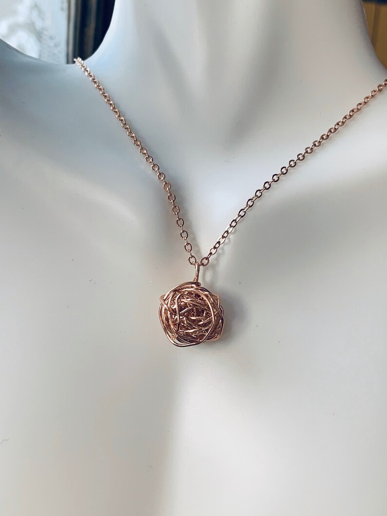 May include: A rose gold necklace with a delicate, intricate pendant made of twisted wire.