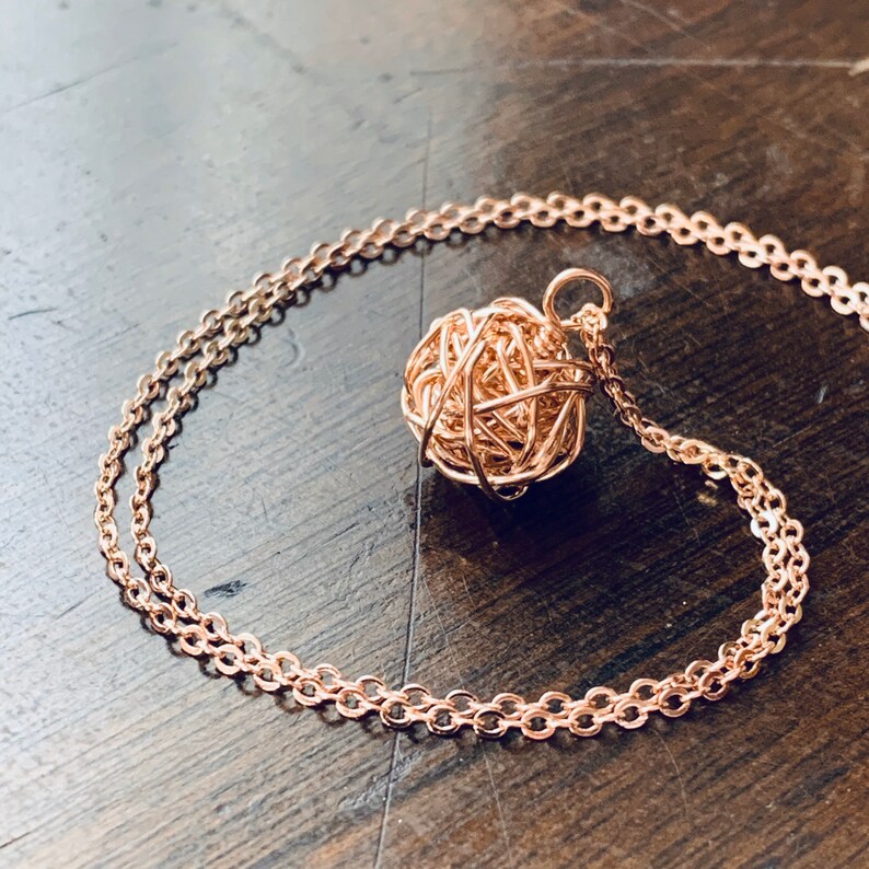 May include: A rose gold necklace with a delicate chain and a wire-wrapped ball pendant.