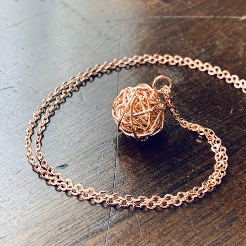 May include: A rose gold necklace with a delicate chain and a wire-wrapped ball pendant.
