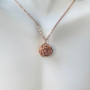 May include: A rose gold chain necklace with a rose gold wire ball pendant.