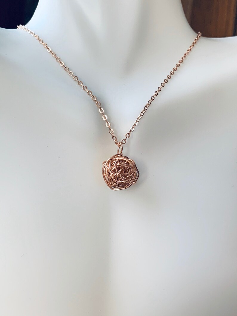 May include: A rose gold chain necklace with a rose gold wire ball pendant.