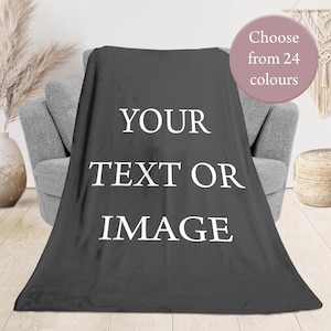 May include: A dark grey rectangular fleece blanket featuring the white text YOUR TEXT OR IMAGE centred on the front. A circular badge in the upper right corner displays the text Choose from 24 colours in white lettering on a mauve background.
