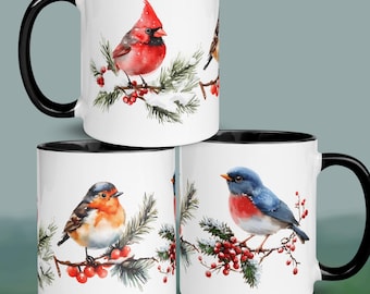 May include: White ceramic mugs with black handles and rims, featuring watercolor illustrations of various birds perched on snow-covered branches with red berries. The birds include a red cardinal, a robin, and a bluebird.
