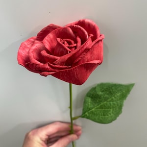 May include: A single red rose with a green leaf, the rose is made of wood and has a realistic appearance.