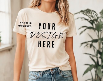 May include: A woman wearing a light beige t-shirt with the text "YOUR DESIGN HERE" printed on the front. She is wearing blue jeans and has long blonde hair.
