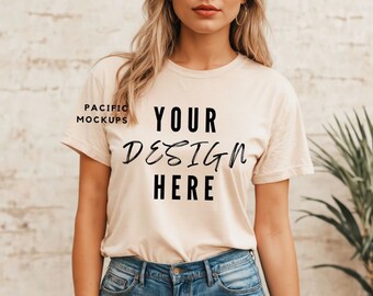 May include: A woman wearing a light beige t-shirt with the text "YOUR DESIGN HERE" printed on the front. She is wearing blue denim shorts and has long blonde hair.