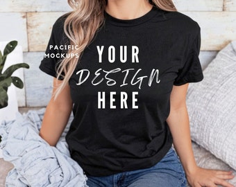 Puede incluir: Camiseta negra con el texto "YOUR DESIGN HERE" en escritura blanca. La camiseta es de manga corta y se lleva con vaqueros azules. La imagen es una maqueta, perfecta para mostrar diseños personalizados.