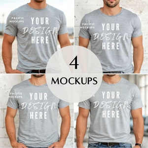Könnte beinhalten: Vier Mockups eines grauen T-Shirts mit dem Text "YOUR DESIGN HERE" auf der Vorderseite. Die T-Shirts werden von einer Person getragen, die vor einer weißen Backsteinwand steht.