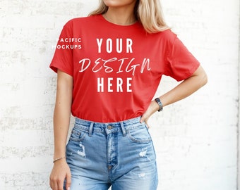May include: A red t-shirt with the text "YOUR DESIGN HERE" in white. The t-shirt is being worn by a person with long blonde hair. The person is wearing blue jeans.