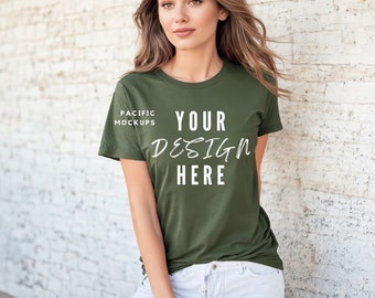 May include: A woman wearing a green t-shirt with the text "YOUR DESIGN HERE" and "PACIFIC MOCKUPS" printed on it. She is standing in front of a white brick wall.