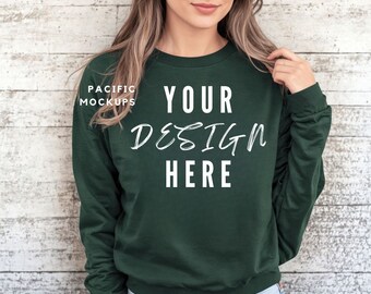 May include: A dark green sweatshirt with long sleeves and a crew neck. The text "YOUR DESIGN HERE" is written in white on the front of the sweatshirt.