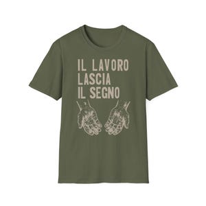 Può includere: Una t-shirt a maniche corte color verde oliva con il testo beige IL LAVORO LASCIA IL SEGNO stampato sopra un'illustrazione grafica di due palmi aperti con dettagliate linee e effetti puntinati sulla superficie della pelle.