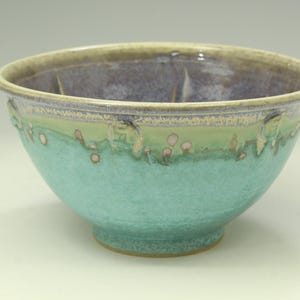 May include: A ceramic bowl featuring a wide, rounded rim and a tapered base. The exterior displays a vibrant turquoise glaze that transitions into a soft green near the top, accented by small, raised circular textures. The interior is a deep purple.