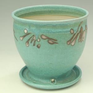 May include: A turquoise ceramic planter with a matching saucer. The planter has a rounded shape with a slightly flared rim and is decorated with brown and white abstract designs. The planter is suitable for indoor or outdoor use.
