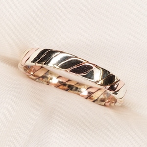 May include: A tri-colour metal ring featuring a twisted rope design. The band is constructed from alternating segments of yellow, rose, and white-toned metal, creating a continuous braided pattern that wraps around the entire circumference of the ring.