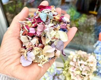 May include: A hand holding a handful of dried flower petals in shades of pink, purple, blue, and white. The text "One handful" is written above the hand.