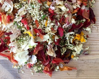 May include: A mix of dried flower petals in shades of red, orange, yellow, white, and pink. The petals are scattered on a wooden surface.