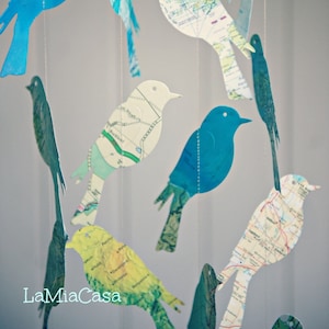 Puede incluir: Un móvil hecho de pájaros de papel con un diseño de mapa. Los pájaros están suspendidos de un techo blanco y están en varios tonos de azul y verde. El móvil es una adición caprichosa y decorativa a cualquier habitación.