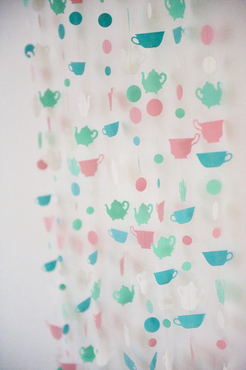May include: A garland of paper cutouts featuring teapots and teacups in shades of green, pink, and white. The garland is strung with small circles in various colors.