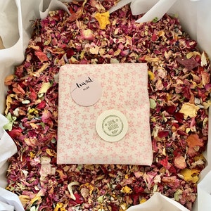 Pu&ograve; includere: Un sacchetto regalo a fantasia rosa e bianca riempito di petali di fiori secchi. Il sacchetto ha due adesivi, uno che dice "Fatto a mano" e l'altro che dice "100% Naturale".