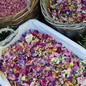 Pu&ograve; includere: Un cesto di vimini bianco pieno di un mix di petali di fiori secchi in tonalit&agrave; di rosa, viola, giallo e bianco.
