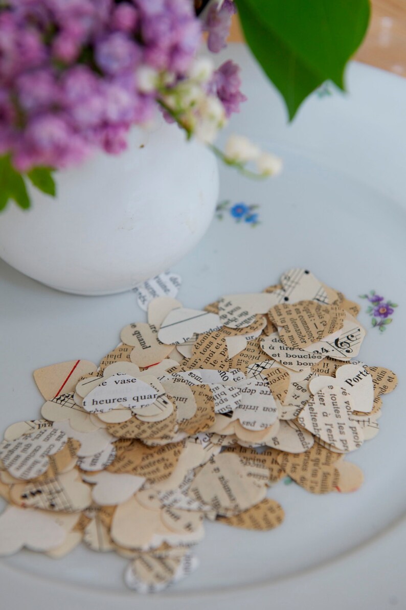 Puede incluir: Un plato blanco con una dispersi&oacute;n de peque&ntilde;os corazones de papel cortados de viejas p&aacute;ginas de libros. Los corazones son de varios tonos de crema y beige, algunos mostrando notas musicales y texto.