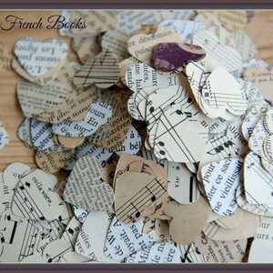 Puede incluir: Un mont&oacute;n de confeti en forma de coraz&oacute;n hecho de p&aacute;ginas de libros franceses antiguos y partituras musicales. El confeti est&aacute; esparcido sobre una superficie de madera. El texto "Vintage French Books" es visible en la parte superior de la imagen.