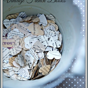 Puede incluir: Un cuenco de cer&aacute;mica blanco lleno de confeti de papel en forma de coraz&oacute;n. El confeti est&aacute; hecho de p&aacute;ginas de libros franceses antiguos y partituras musicales. El cuenco est&aacute; sobre una tela de lunares blancos y grises.