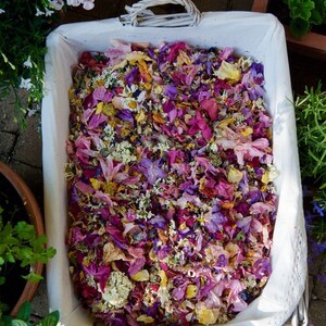 Pu&ograve; includere: Un cesto di vimini bianco pieno di un mix di petali di fiori secchi in tonalit&agrave; di rosa, viola e giallo. I petali sono disposti in modo casuale e creano una bella e colorata esposizione.