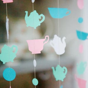 May include: A string of paper cutouts hanging from the ceiling. The cutouts are in the shape of teapots, cups, and circles. The colors are pink, blue, green, and white.