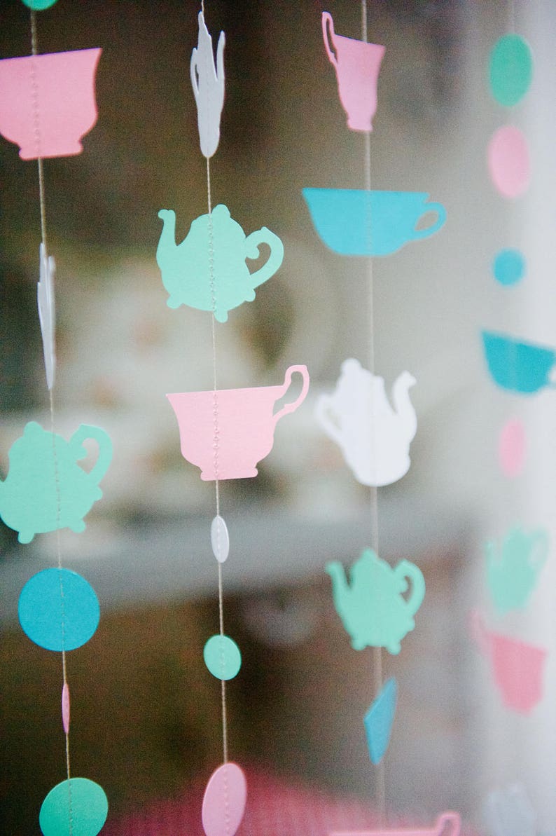 May include: A string of paper cutouts hanging from the ceiling. The cutouts are in the shape of teapots, cups, and circles. The colors are pink, blue, green, and white.