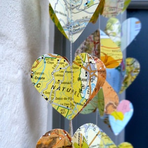 May include: A string of heart-shaped ornaments made from maps. Each heart features a different section of a map with various geographical features, including rivers, roads, and towns. The hearts are strung together with white thread and hang from a white ceiling.