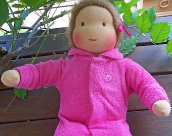 May include: A pink, soft, plush doll wearing a pink hooded jumpsuit. The doll has brown hair and a painted face.