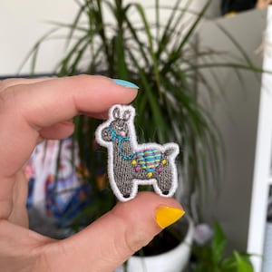 May include: A grey embroidered llama patch with a colourful saddle and a white outline.