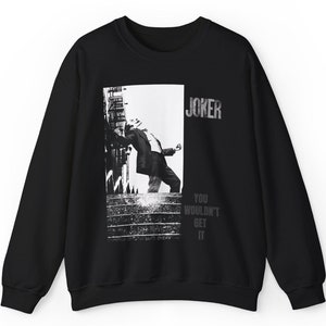 May include: Black sweatshirt featuring a grayscale image of a person leaning against a building, with the word "JOKER" above and "YOU WOULDN'T GET IT" below. The sweatshirt is made of a soft material.