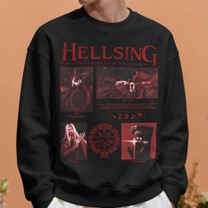 May include: A black long-sleeve sweatshirt featuring a red graphic print from the anime Hellsing. The design includes the title Hellsing, character illustrations of The Baskerville, Alucard, Integra, and Alexander, along with a pentagram symbol.