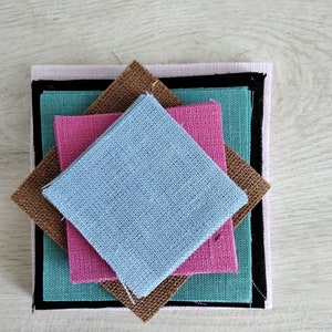 Puede incluir: Una pila de cuatro cuadrados de tela en diferentes colores y texturas. El cuadrado superior es azul claro, el segundo es rosa, el tercero es verde azulado y el inferior es marrón.