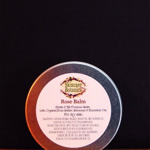 Puede incluir: Una lata blanca con una etiqueta rosa que dice "Skincare Botanics Rose Balm Gentle & all Purpose Balm with Organic Shea Butter, Beeswax & Essential Oils For dry skin" y enumera los ingredientes y las instrucciones de uso.