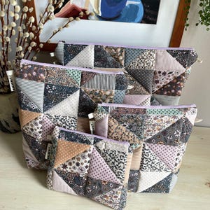 Può includere: Quattro pochette con cerniera patchwork di varie dimensioni. Le pochette presentano un mix di tessuti floreali, a righe e tinta unita nei toni del rosa, grigio e marrone. Ogni pochette ha una cerniera lavanda e una piccola etichetta "NALAKNIT-".