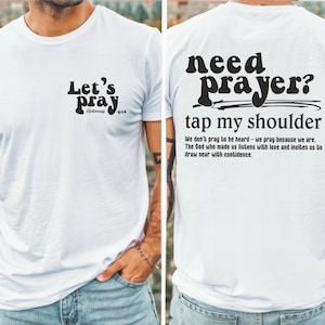 May include: White t-shirt with black text on the front and back. The front says "Let's pray" with "Hebrews 4:16" below. The back says "need prayer? tap my shoulder" with a short message below.