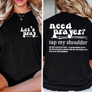 May include: Black t-shirt with white text. The front says "Let's Pray" with "Hebrews 4:10" below. The back says "need prayer? tap my shoulder" with a quote below. Religious apparel.