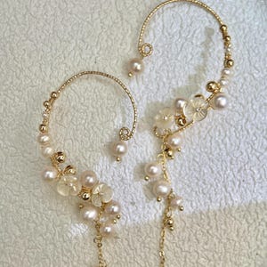 May include: A pair of gold ear cuffs with pearl and flower accents. The cuffs are made of thin wire and have a delicate, feminine look.