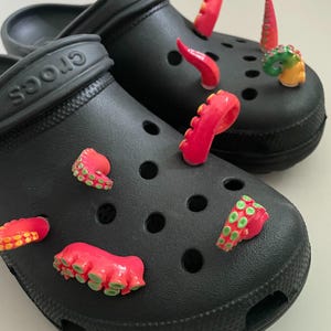 Könnte beinhalten: Schwarze Crocs mit rosa und grünen Tintenfisch-Anhängern, die an den Löchern befestigt sind. Die Anhänger sind 3D und haben ein realistisches Aussehen.