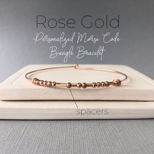 May include: Rose gold personalized Morse code bangle bracelet with small beads and spacers.