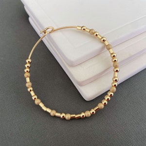 Peut inclure: Un bracelet jonc en or avec des perles texturées. Le bracelet est fait d'un fil fin avec de petites perles rondes.
