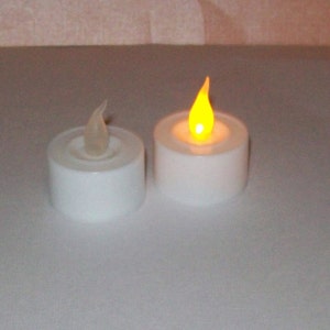 May include: Two white LED tea lights with a realistic flickering flame. The tea lights are on a white surface.