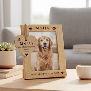 May include: A light wooden photo frame displaying a golden retriever. The frame is inscribed with the name "Molly" and the phrase "You left a paw print on our hearts." A heart-shaped tag is also attached.