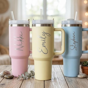 May include: Three pastel-coloured personalised tumblers: pink, yellow, and blue. Each tumbler has a handle, a silver lid, and a straw. The names "Nikki", "Emily", and "Stephen" are printed on the tumblers.