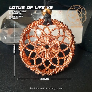 Puede incluir: Un colgante circular hecho de alambre de cobre trenzado con un patrón geométrico de loto, suspendido por un cordón negro con una cuenta dorada. El texto dice LOTUS OF LIFE V2, SACRED CUBIT 144MHZ, LOST CUBIT 177MHZ y dimensiones de 50mm.