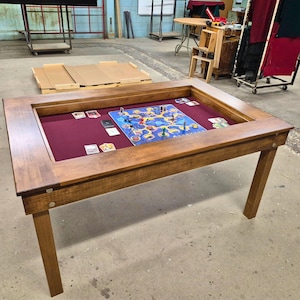 May include: A wooden game table with a raised inset for playing board games. The table has a dark wood stain and a red felt lining. A board game is set up on the table.